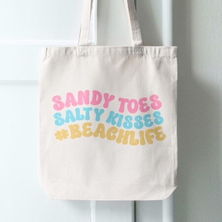 A beach life themed tote bag featuring a free SVG file design saying "sandy toes salty kisses.